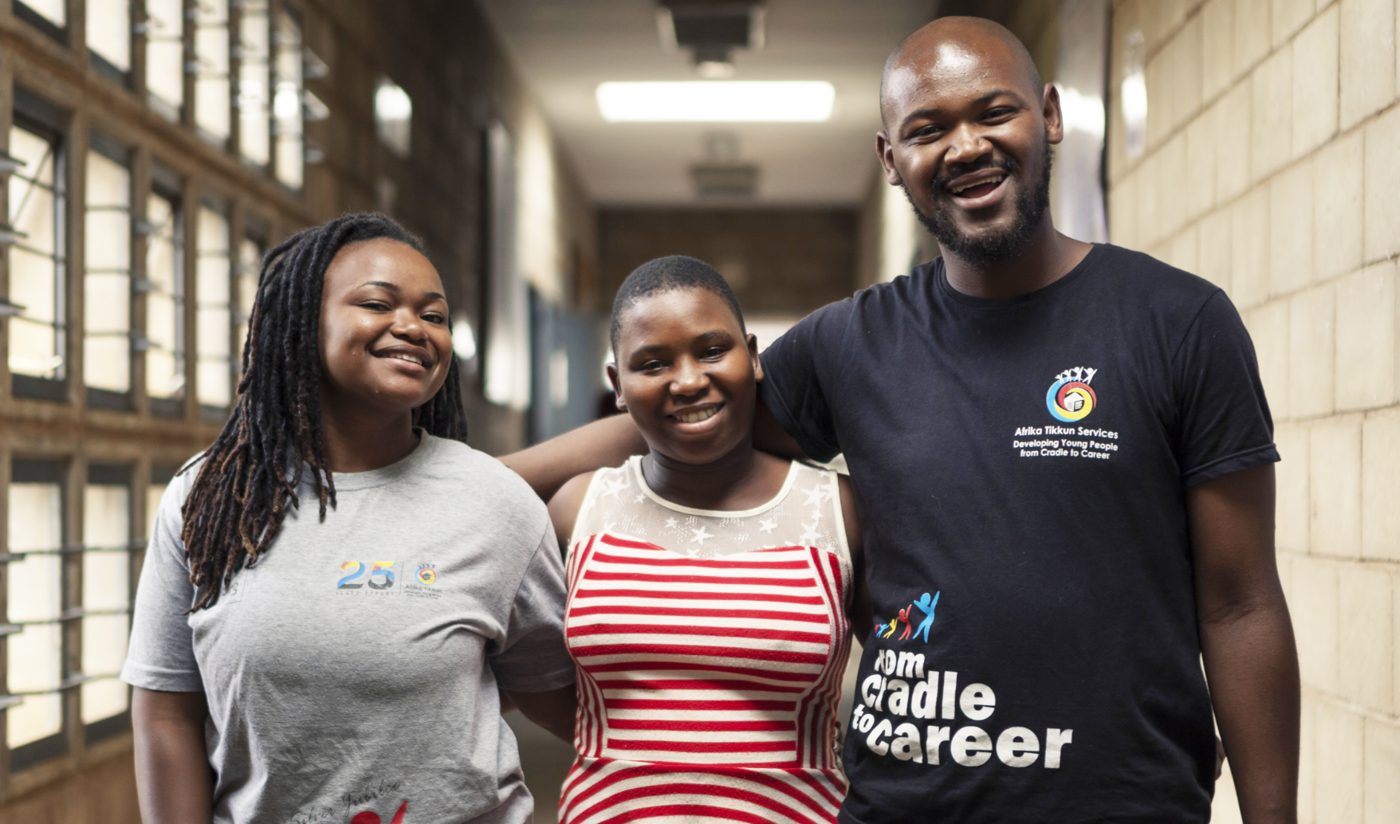 A teacher smiling with two learners in a school hallway