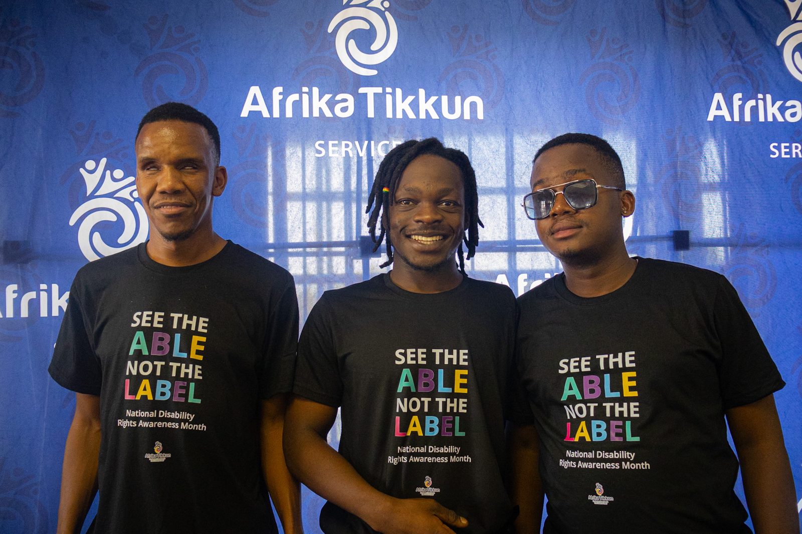 Three young men in front of an Afrika Tikkun banner